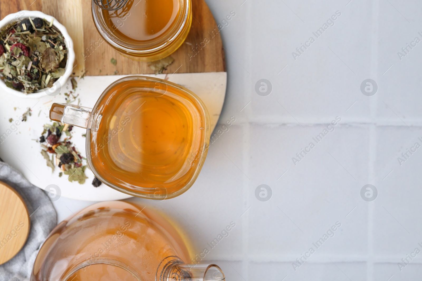 Photo of Delicious herbal tea with honey and dry leaves on white tiled table, flat lay. Space for text