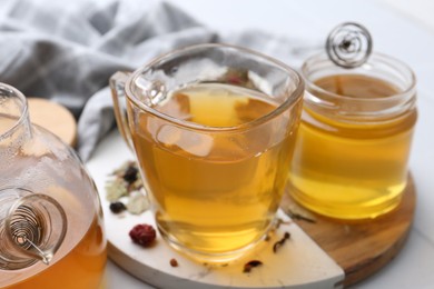 Photo of Delicious herbal tea with honey and dry leaves on white table, closeup