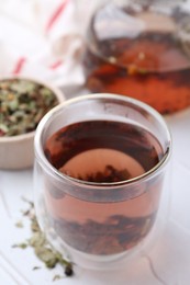 Photo of Delicious herbal tea and dry leaves on white table, closeup