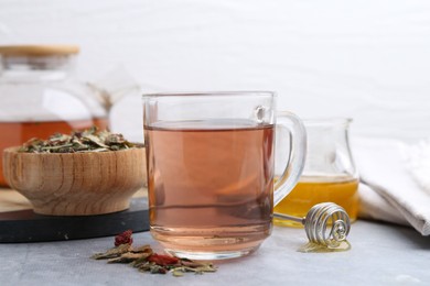 Photo of Delicious herbal tea with honey and dry leaves on grey table