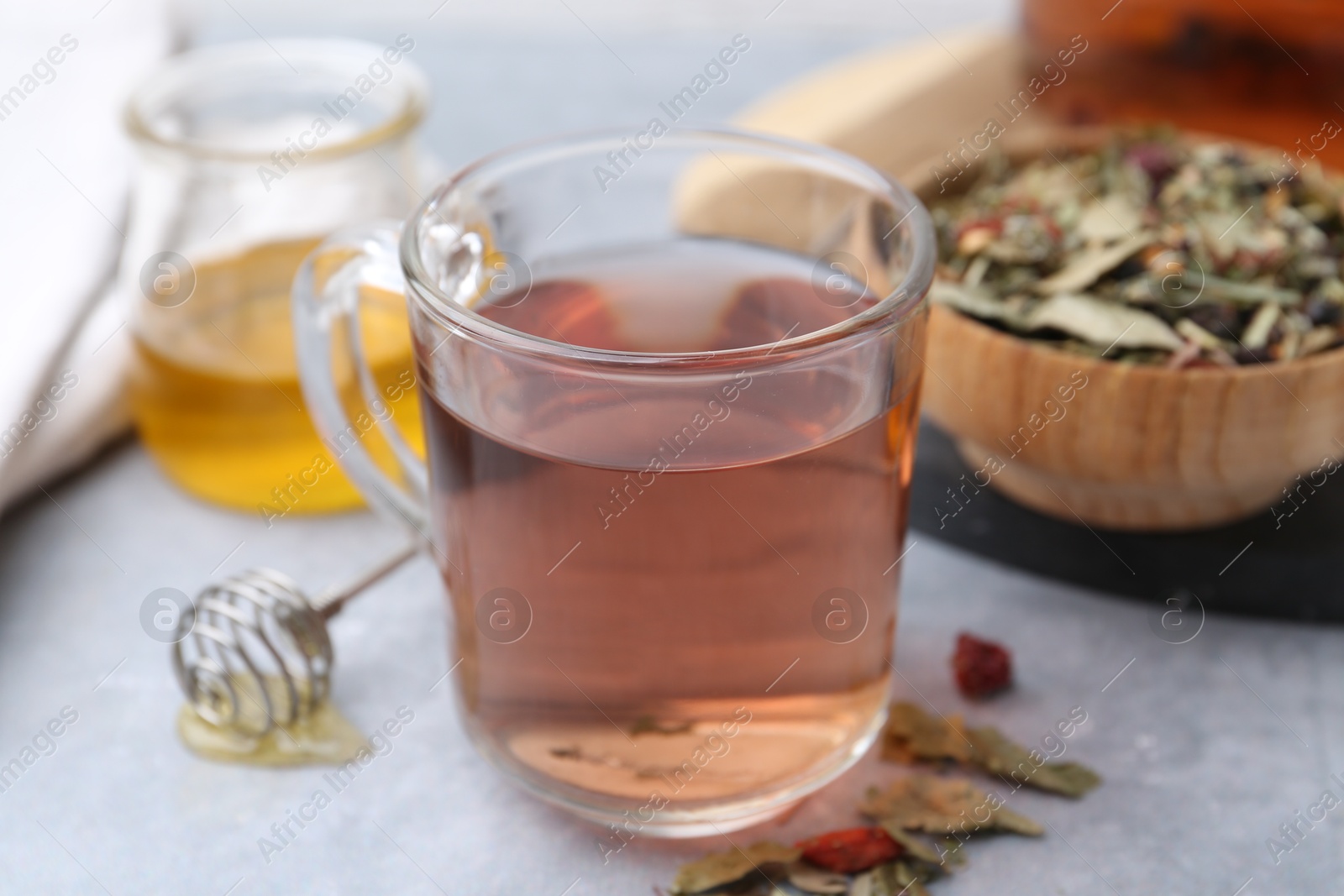 Photo of Delicious herbal tea with honey and dry leaves on grey table, closeup