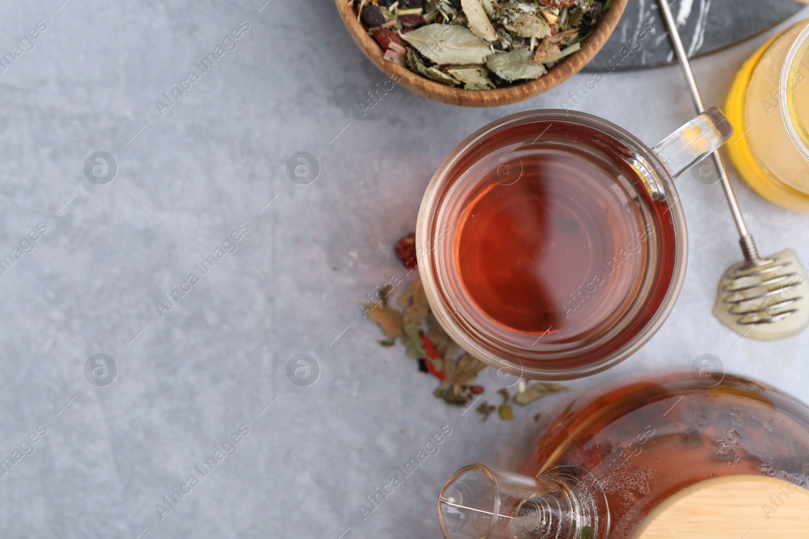 Photo of Delicious herbal tea with honey and dry leaves on grey table, flat lay. Space for text