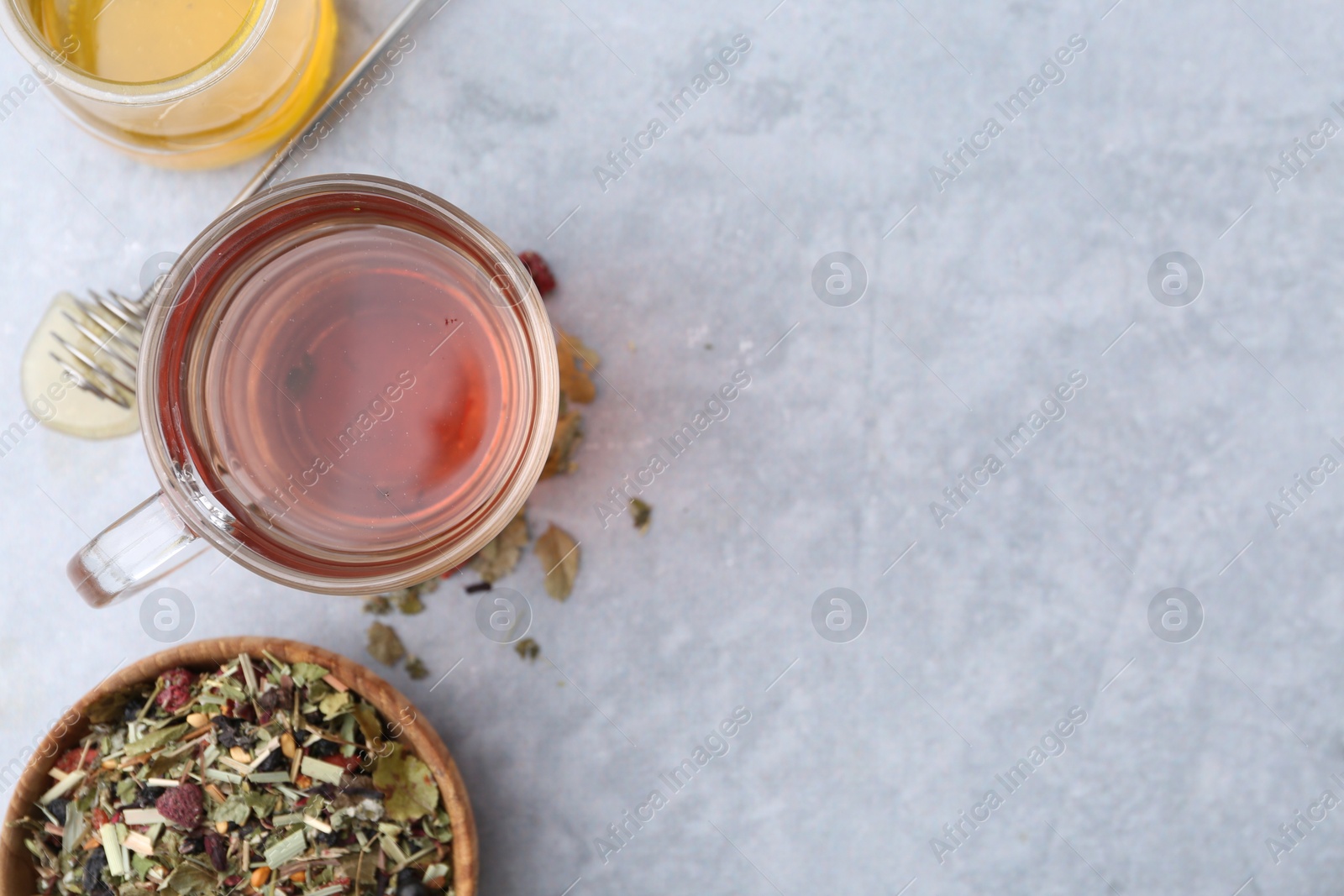 Photo of Delicious herbal tea with honey and dry leaves on grey table, flat lay. Space for text