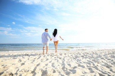 Photo of Happy couple running together on beach, back view