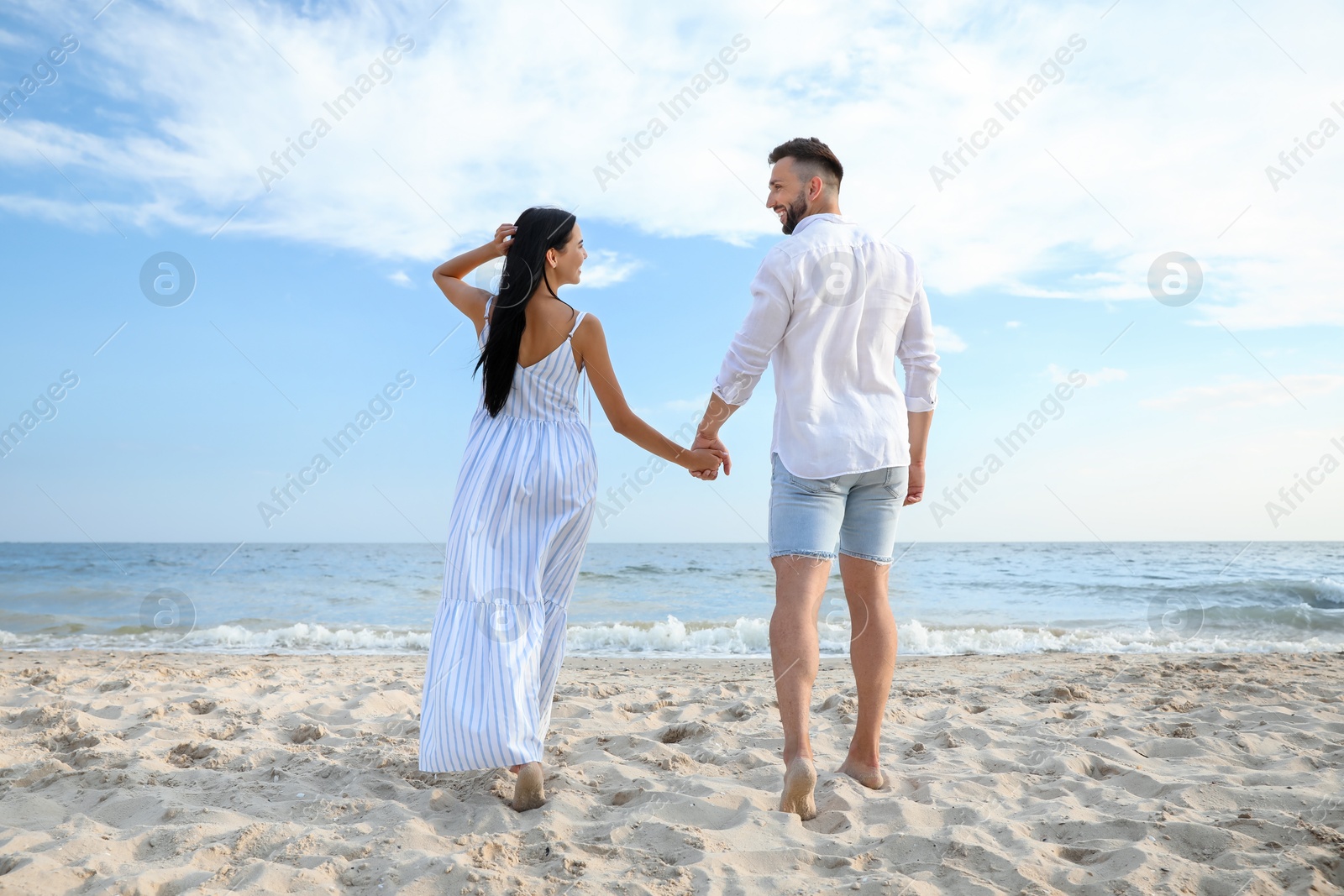 Photo of Happy young couple walking together on beach, back view