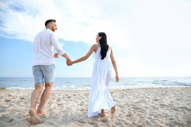 Photo of Happy young couple walking together on beach, back view