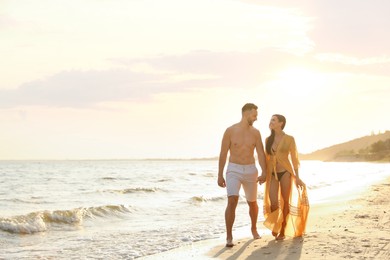 Photo of Happy young couple walking together on beach at sunset