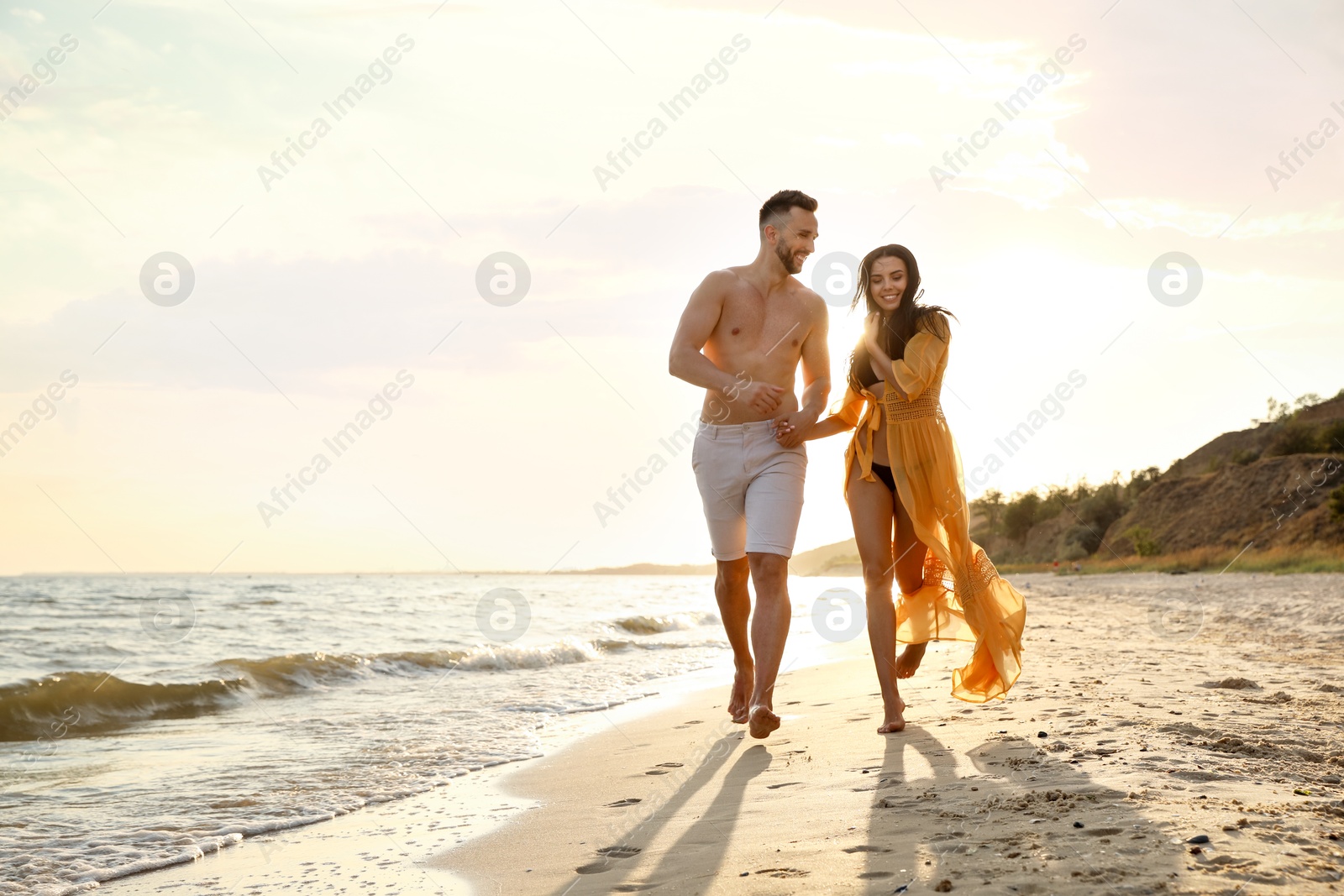 Photo of Happy young couple running together on beach at sunset