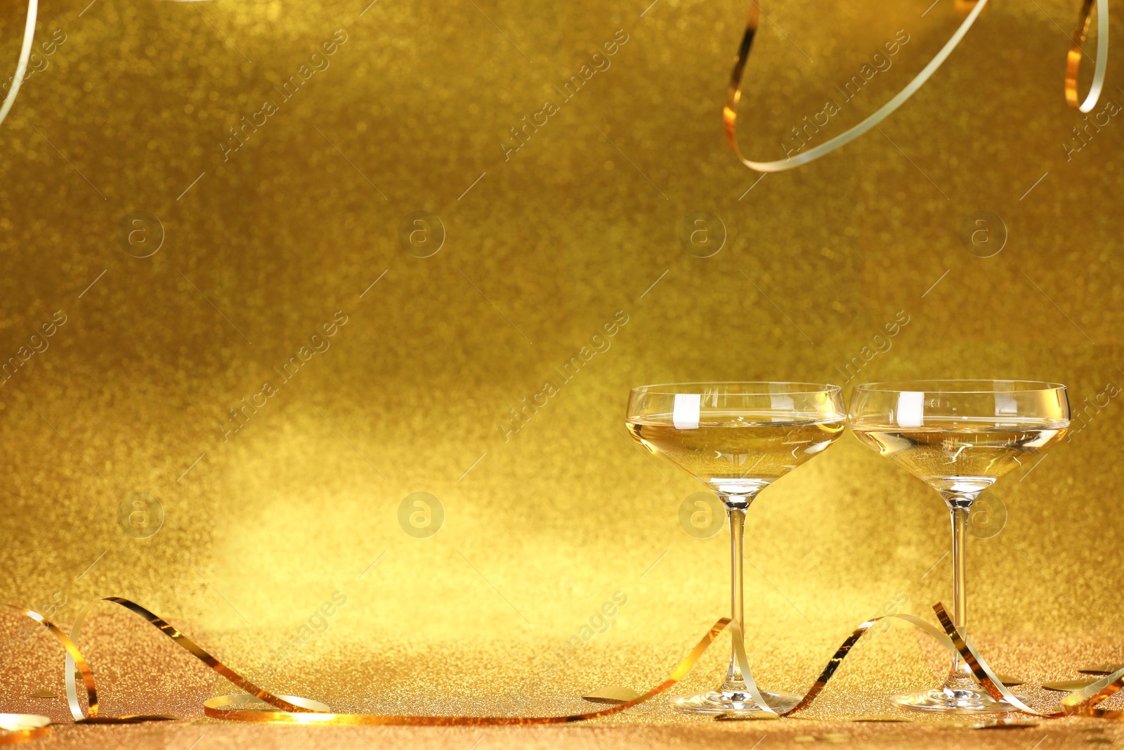 Photo of Champagne in glasses and streamers on golden background. Space for text