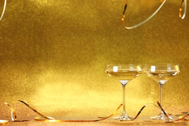 Photo of Champagne in glasses and streamers on golden background. Space for text