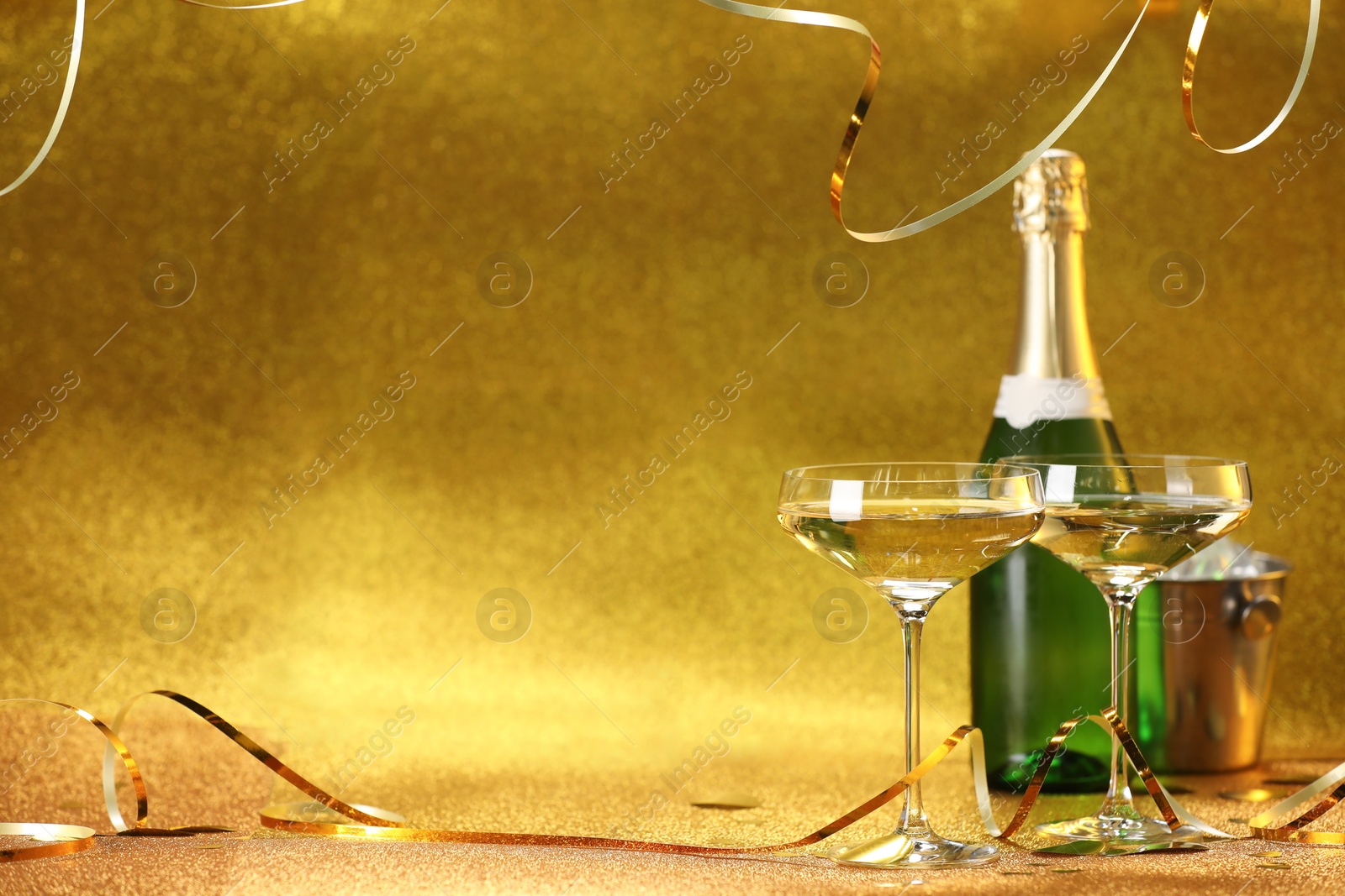 Photo of Champagne in glasses, bottle and ice bucket on golden background. Space for text