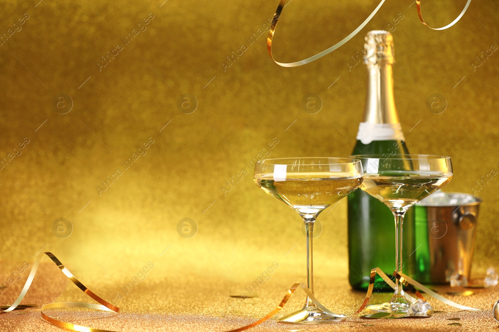 Photo of Champagne in glasses, bottle and ice bucket on golden background. Space for text