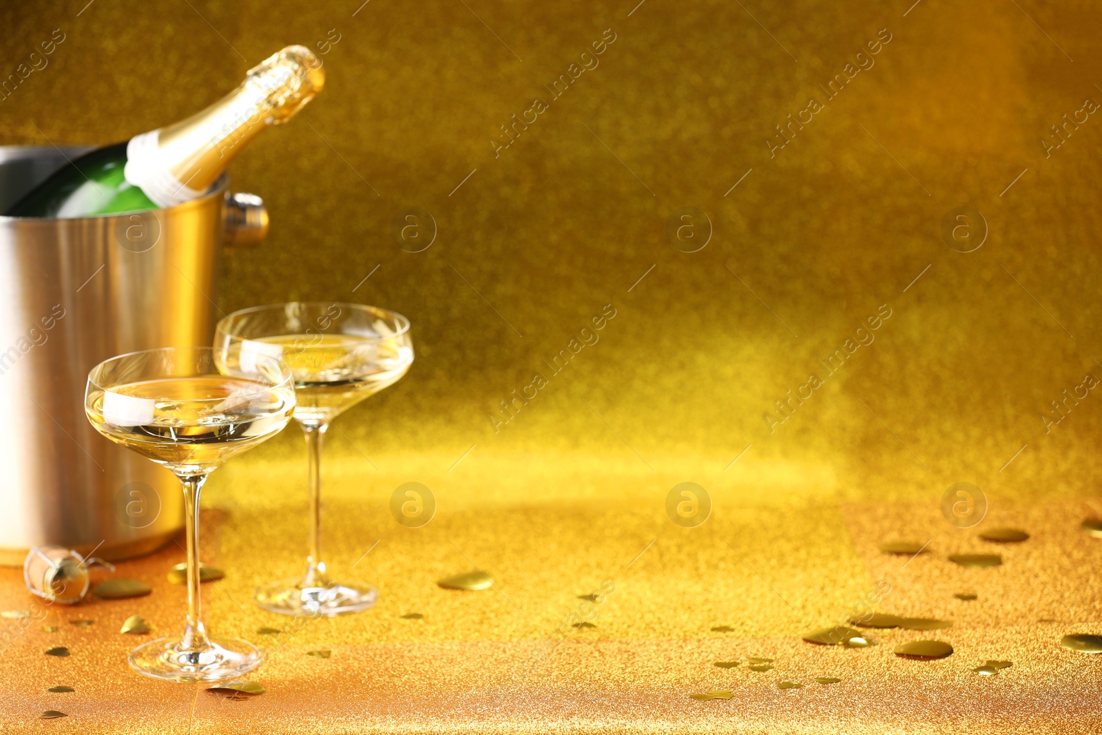 Photo of Champagne in glasses and ice bucket with bottle on golden background. Space for text