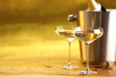 Photo of Champagne in glasses and ice bucket with bottle on golden background. Space for text