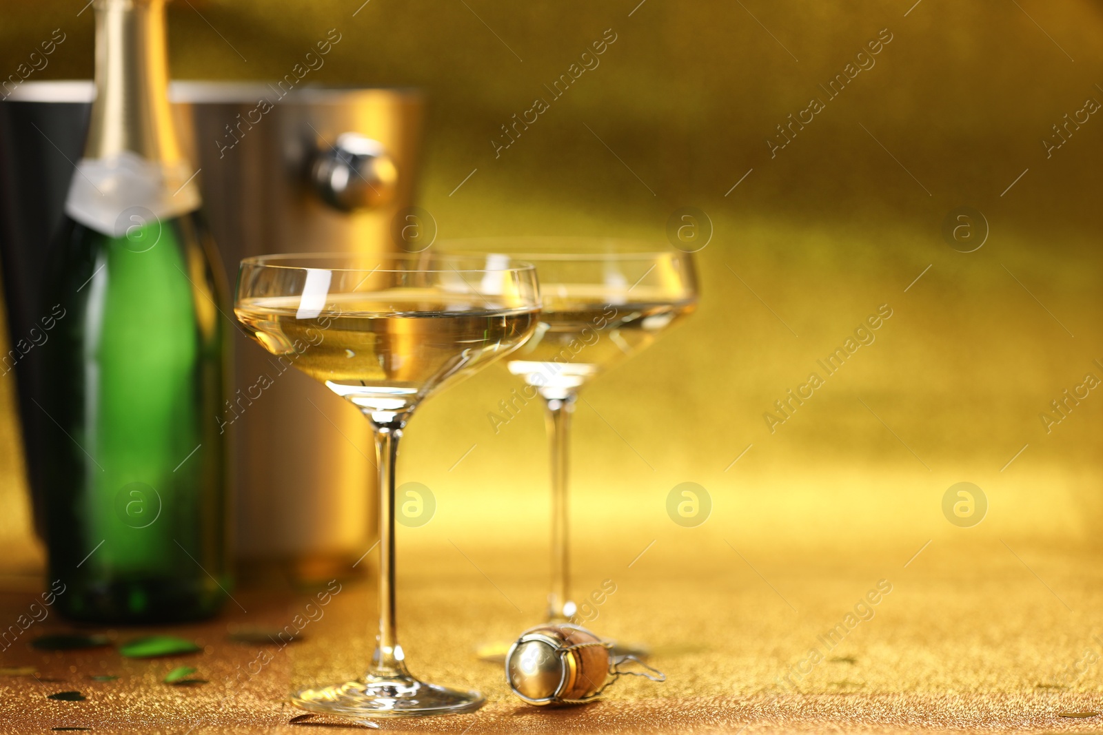 Photo of Champagne in glasses, bottle and ice bucket on golden background. Space for text