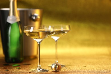 Photo of Champagne in glasses, bottle and ice bucket on golden background. Space for text