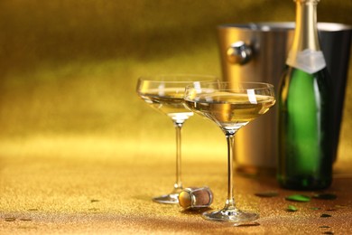 Photo of Champagne in glasses, bottle and ice bucket on golden background. Space for text