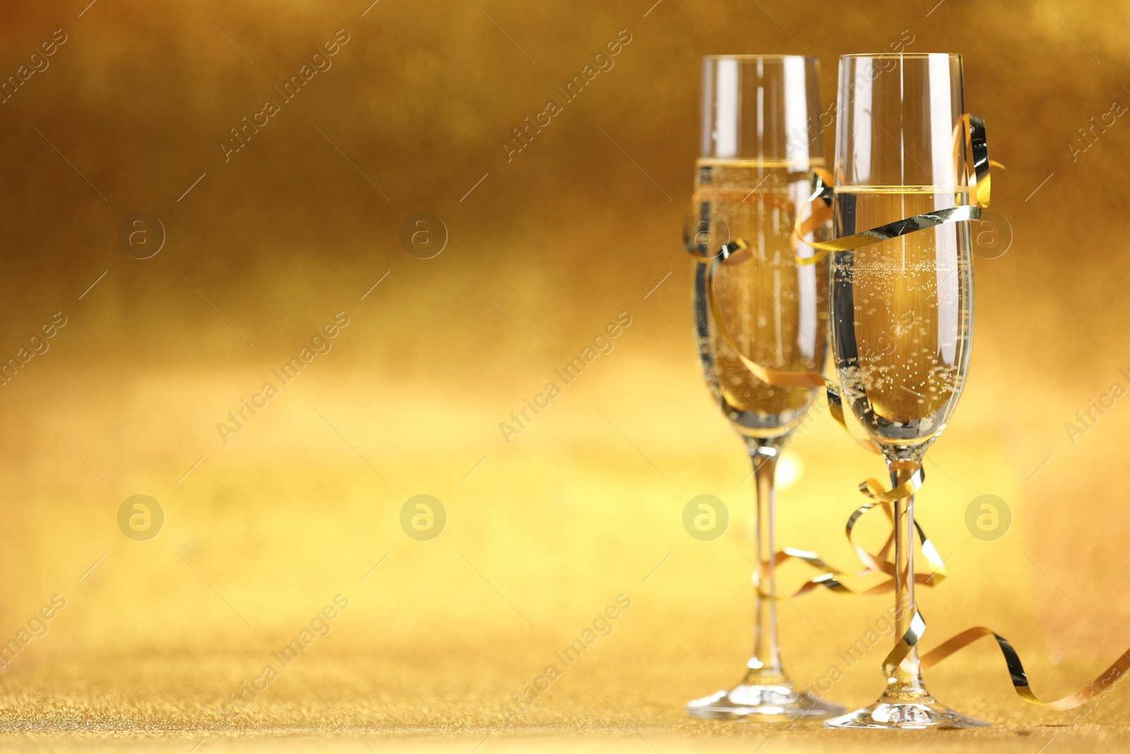 Photo of Champagne in glasses and streamers on golden background. Space for text