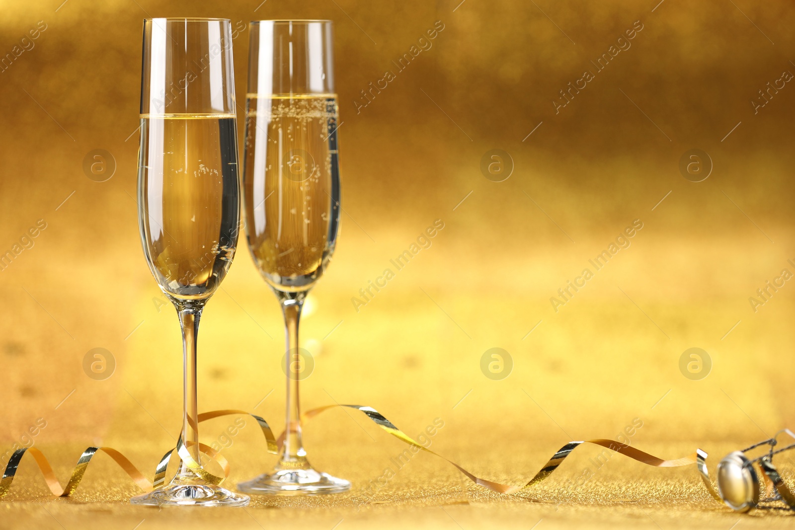 Photo of Champagne in glasses and streamers on golden background. Space for text