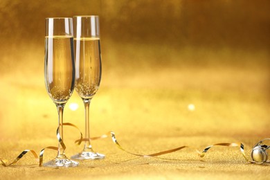 Photo of Champagne in glasses and streamers on golden background. Space for text