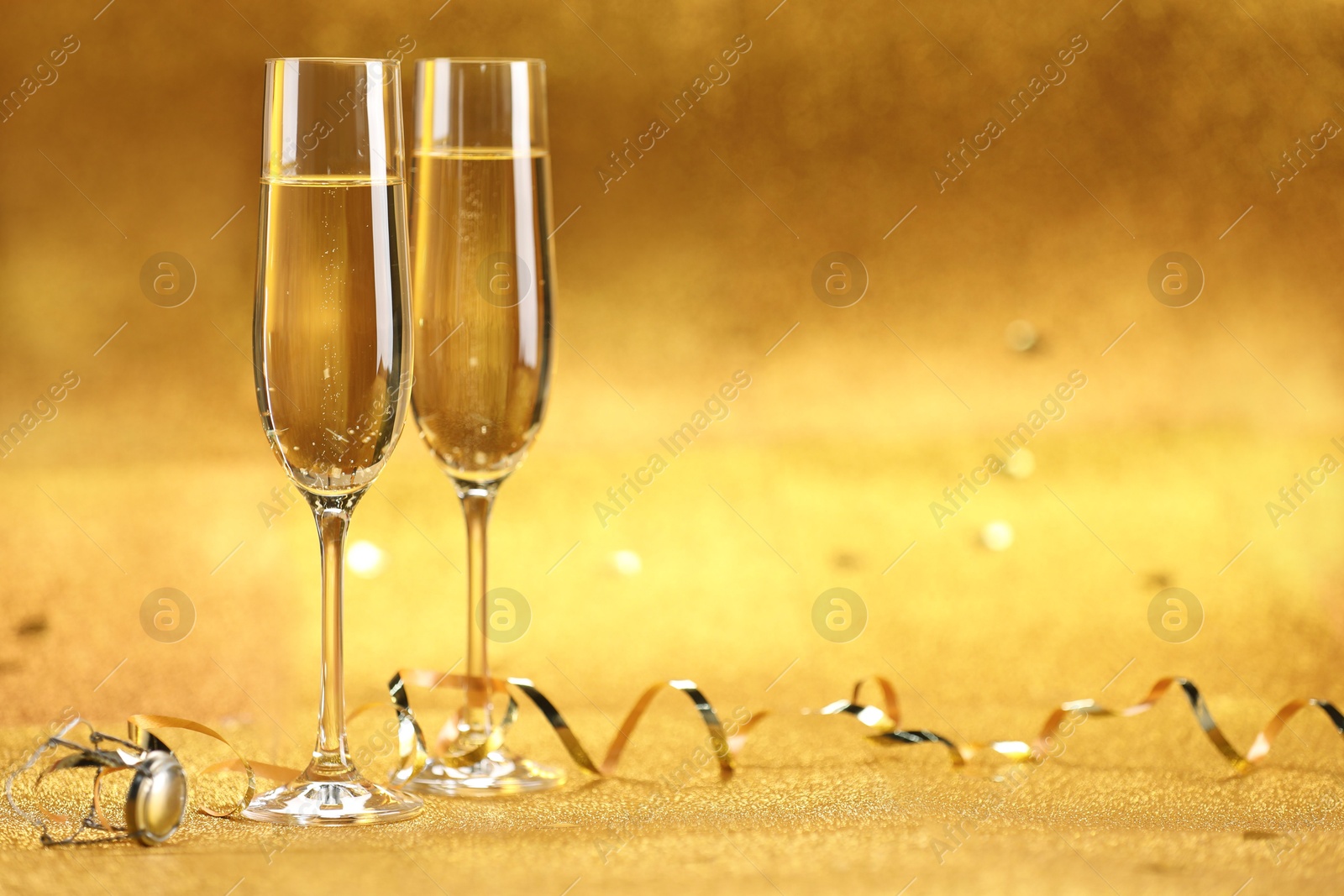 Photo of Champagne in glasses and streamers on golden background. Space for text