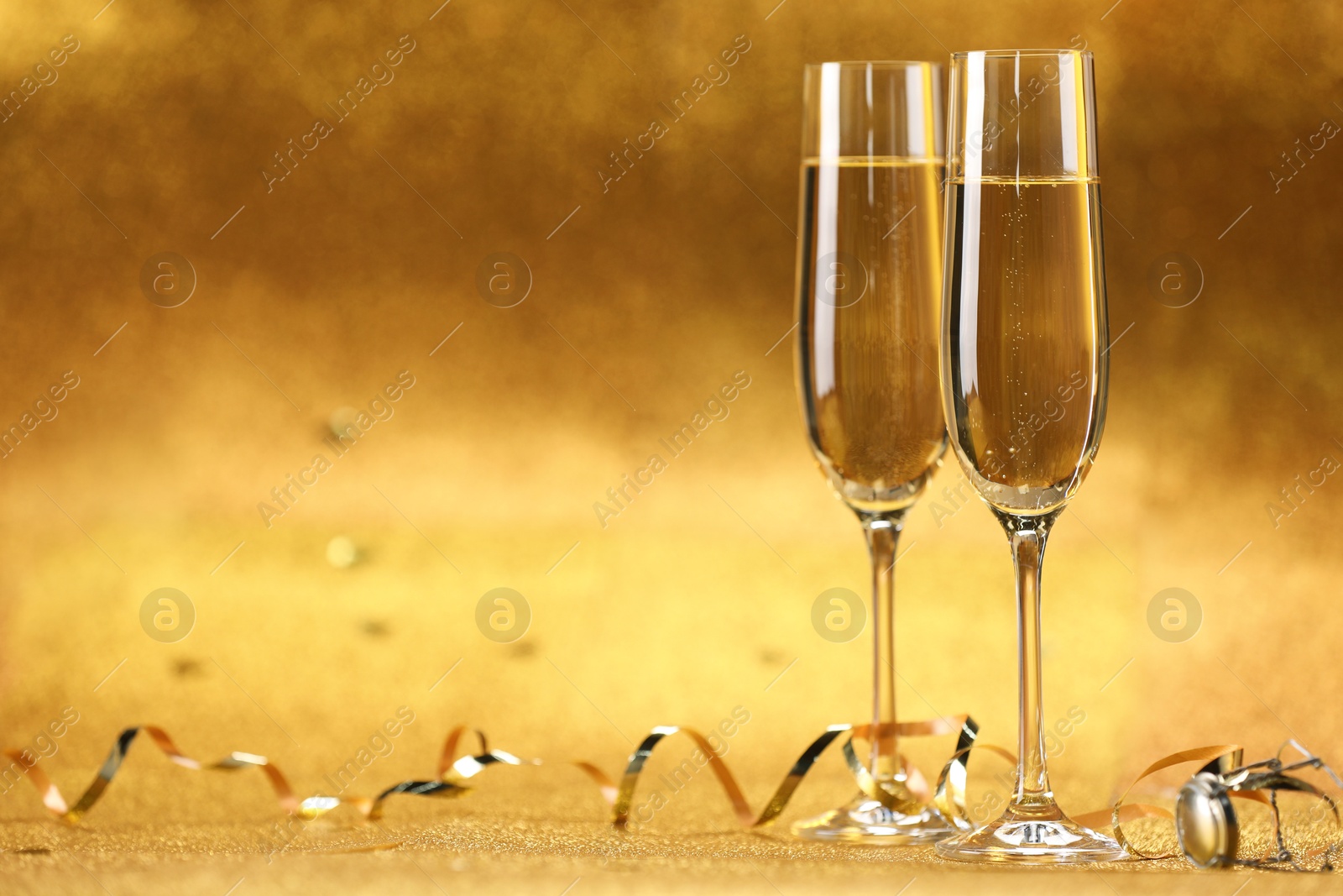 Photo of Champagne in glasses and streamers on golden background. Space for text