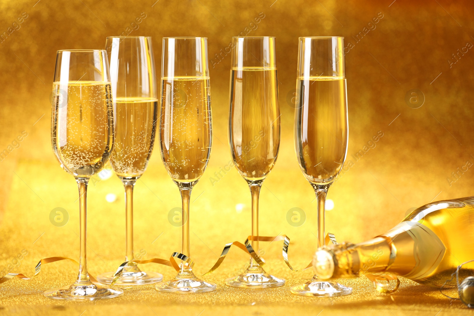 Photo of Champagne in glasses, bottle and streamers on golden background