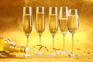 Photo of Champagne in glasses, bottle and streamers on golden background