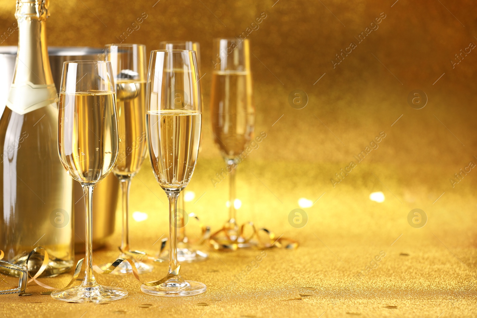 Photo of Champagne, bottle, ice bucket and streamers on golden background. Space for text