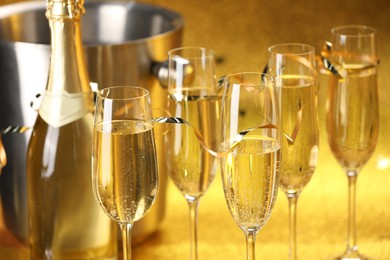 Photo of Champagne in glasses, bottle and ice bucket on golden background, closeup