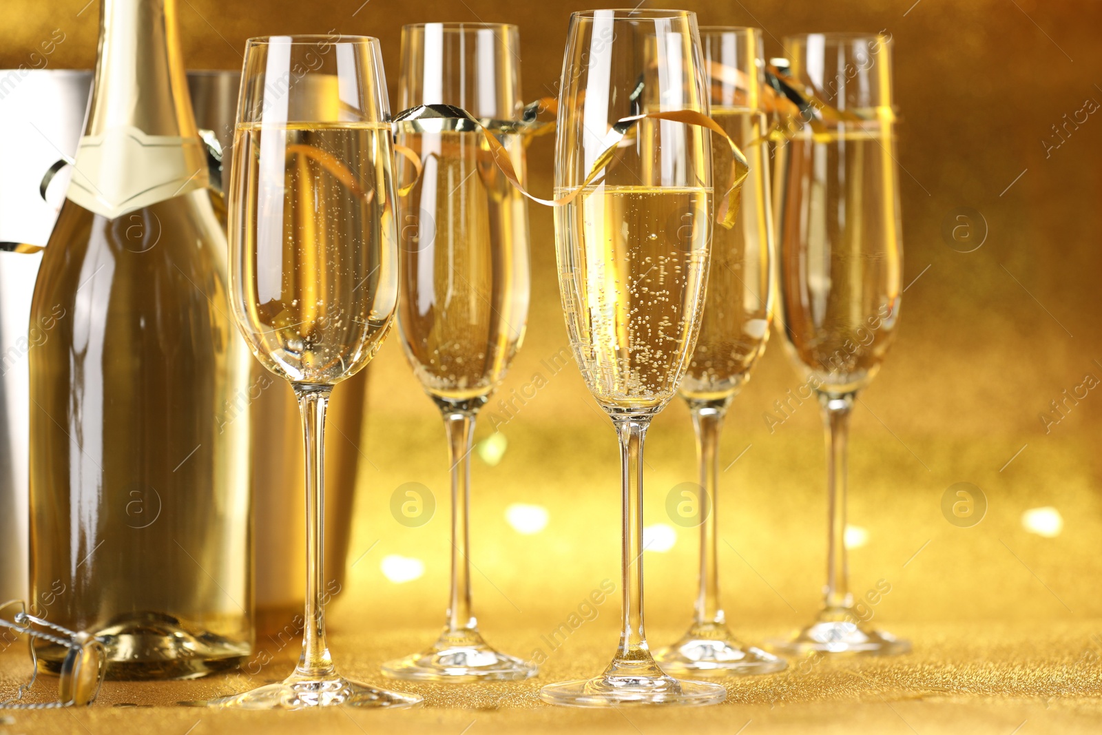 Photo of Champagne in glasses, bottle and ice bucket on golden background, closeup