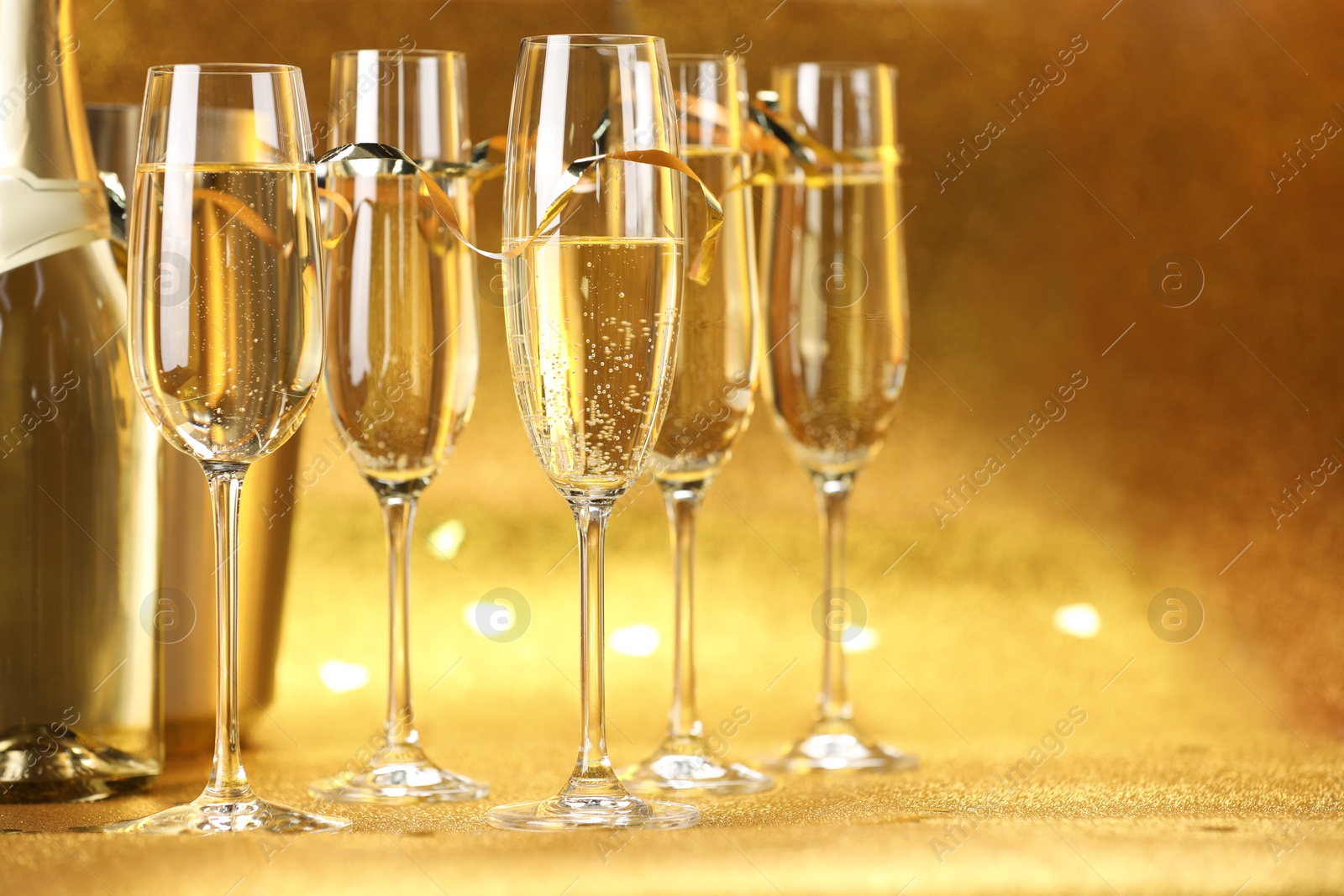 Photo of Champagne, bottle and ice bucket on golden background, closeup. Space for text