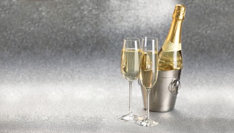 Photo of Champagne in glasses and ice bucket with bottle on silver background. Space for text