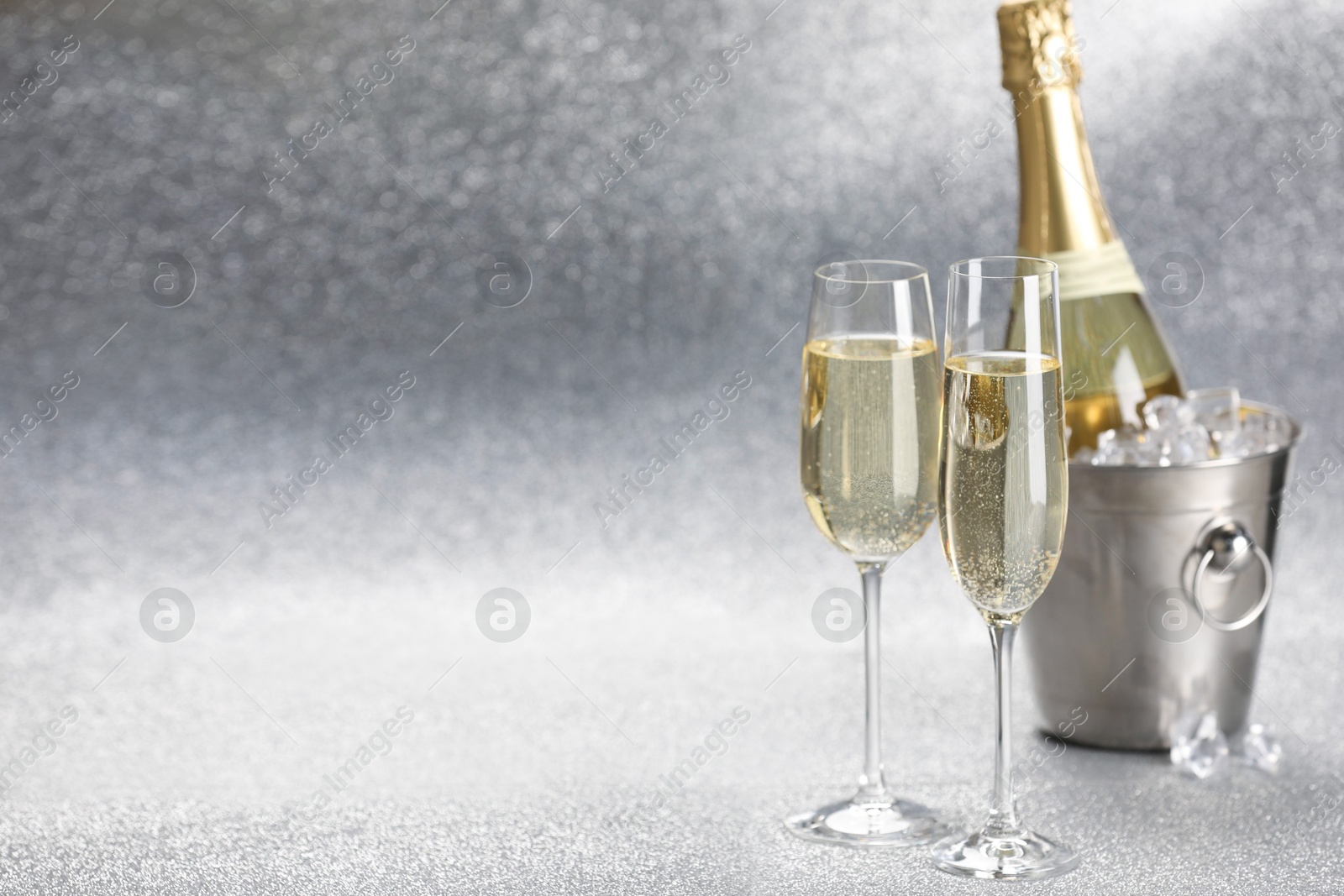 Photo of Champagne in glasses and ice bucket with bottle on silver background. Space for text