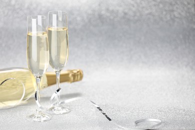 Photo of Champagne in glasses and bottle on silver background. Space for text