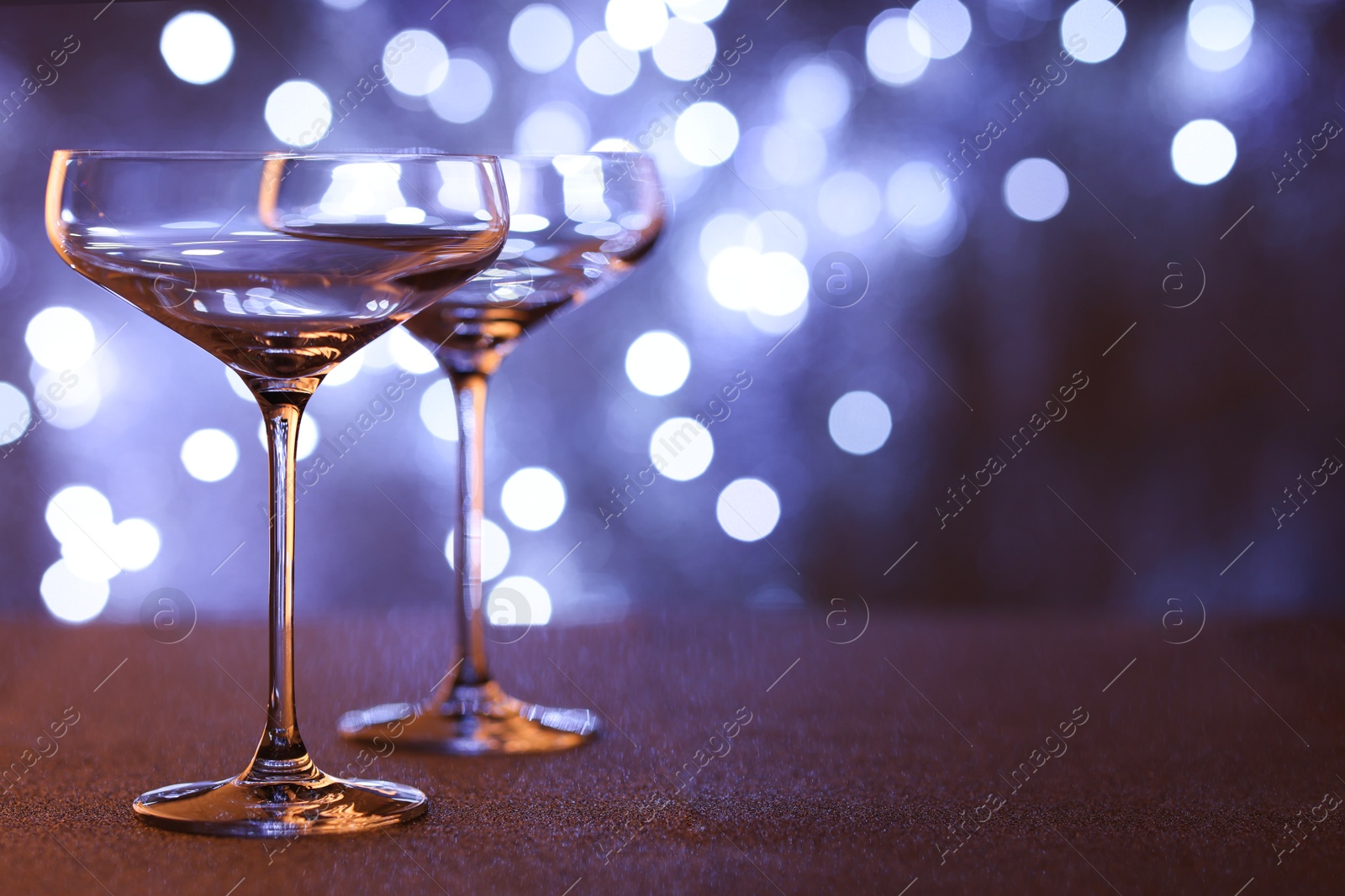 Photo of Champagne in glasses on table against blurred lights. Space for text