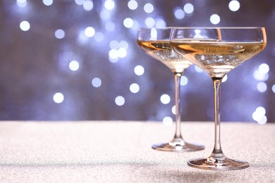 Photo of Champagne in glasses on shiny surface against blurred lights. Space for text