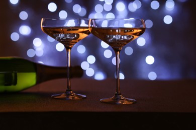 Photo of Champagne in glasses and bottle on table against dark background with blurred lights