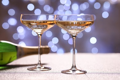 Photo of Champagne in glasses and bottle on shiny surface against blurred lights, closeup