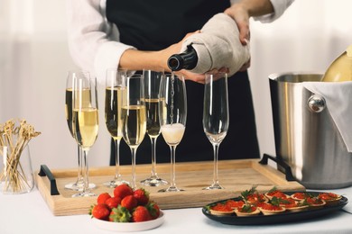 Photo of Waiter filling glasses with champagne indoors, closeup