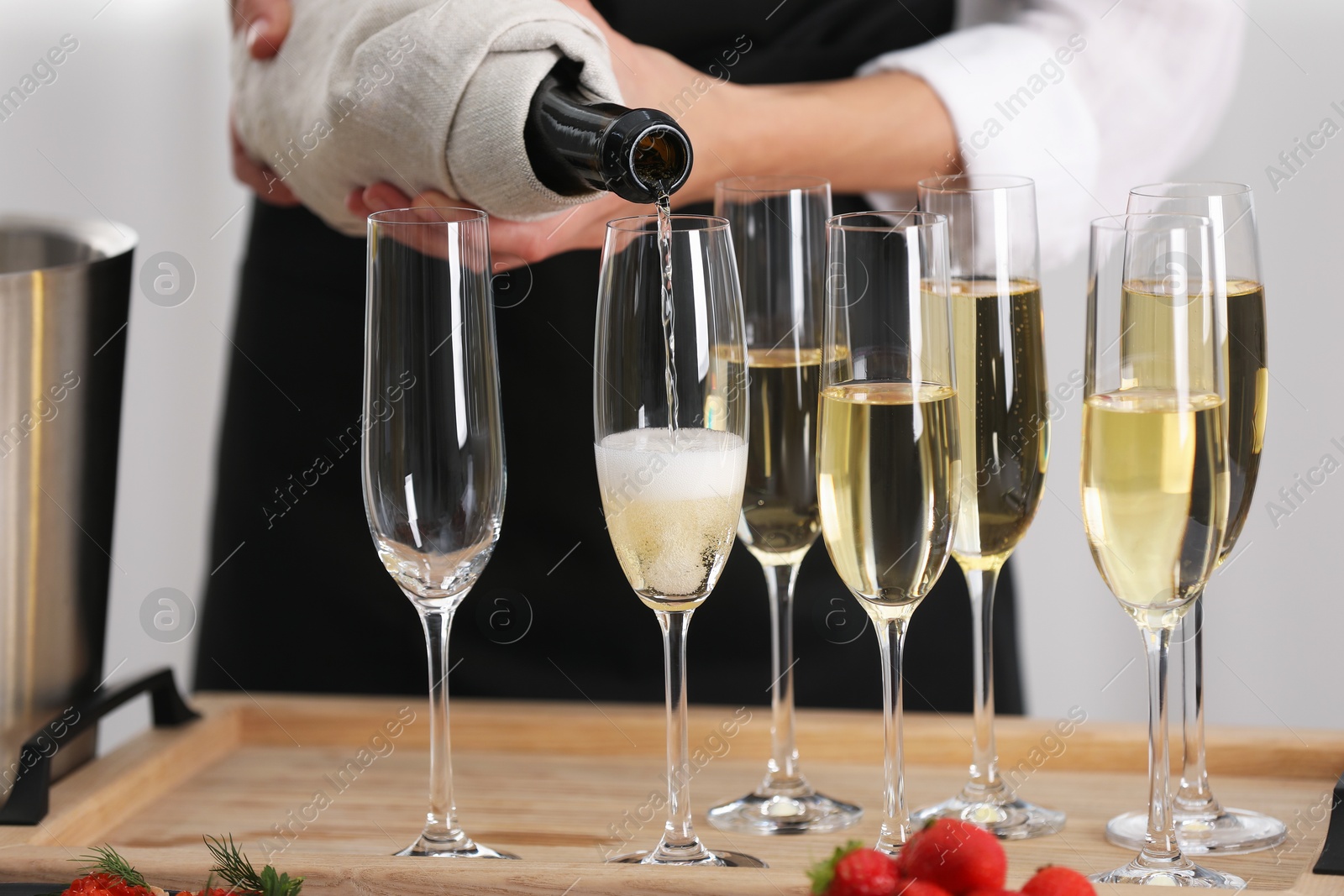 Photo of Waiter filling glasses with champagne indoors, closeup