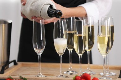 Photo of Waiter filling glasses with champagne indoors, closeup