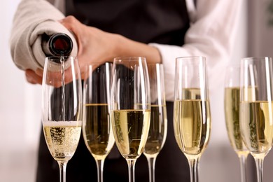 Photo of Waiter filling glasses with champagne indoors, closeup