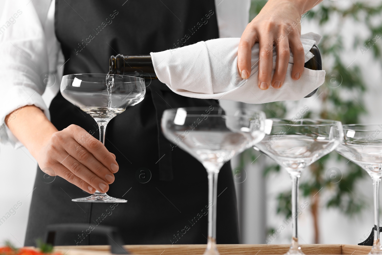 Photo of Waiter filling glasses with champagne indoors, closeup