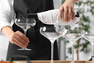 Photo of Waiter filling glasses with champagne indoors, closeup