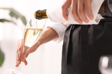 Photo of Waiter pouring champagne into glass indoors, closeup