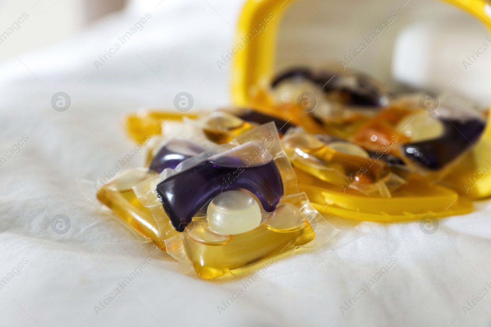 Photo of Laundry detergent capsules in container on white fabric, closeup