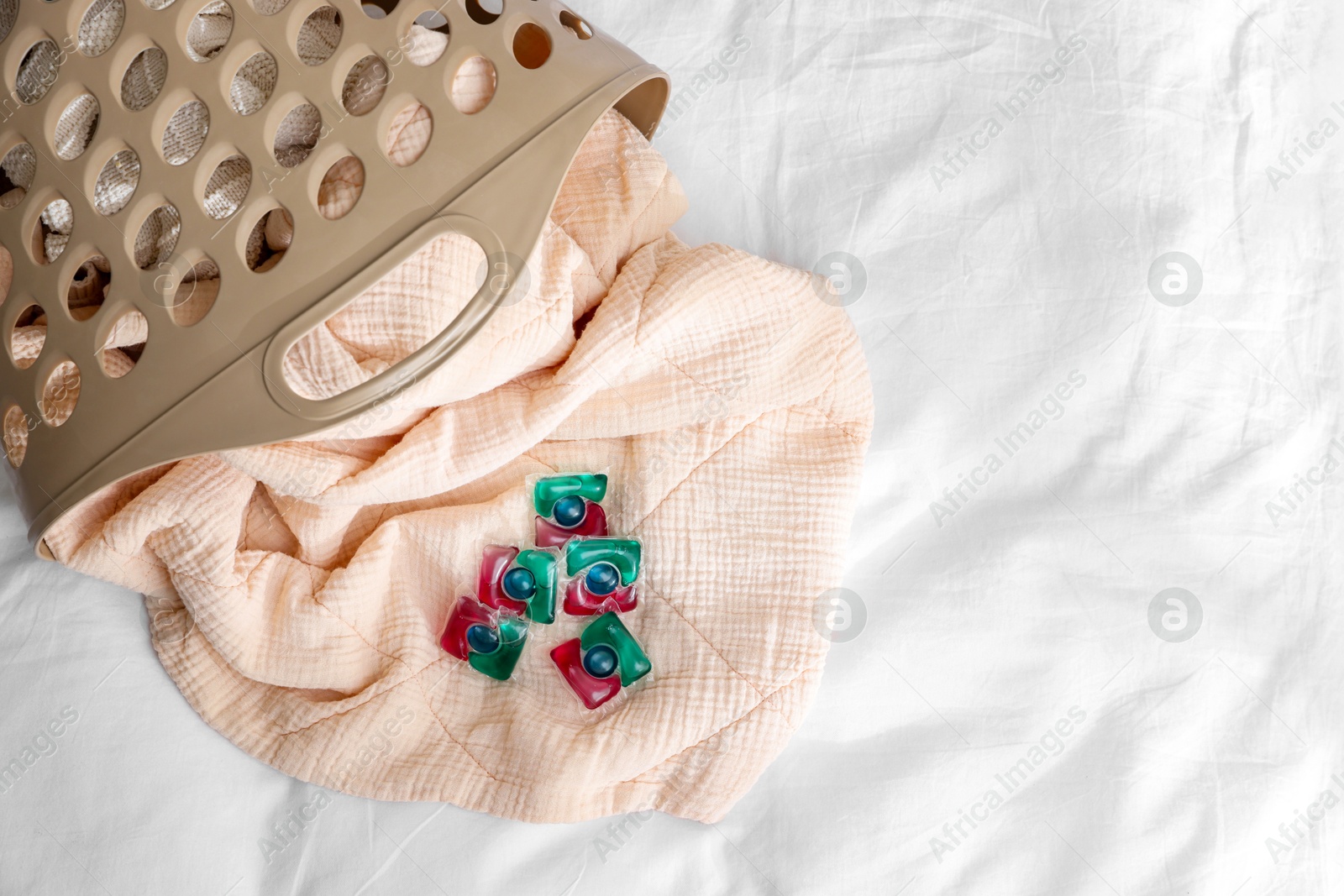 Photo of Laundry detergent capsules and basket with clean linens on bed, top view. Space for text