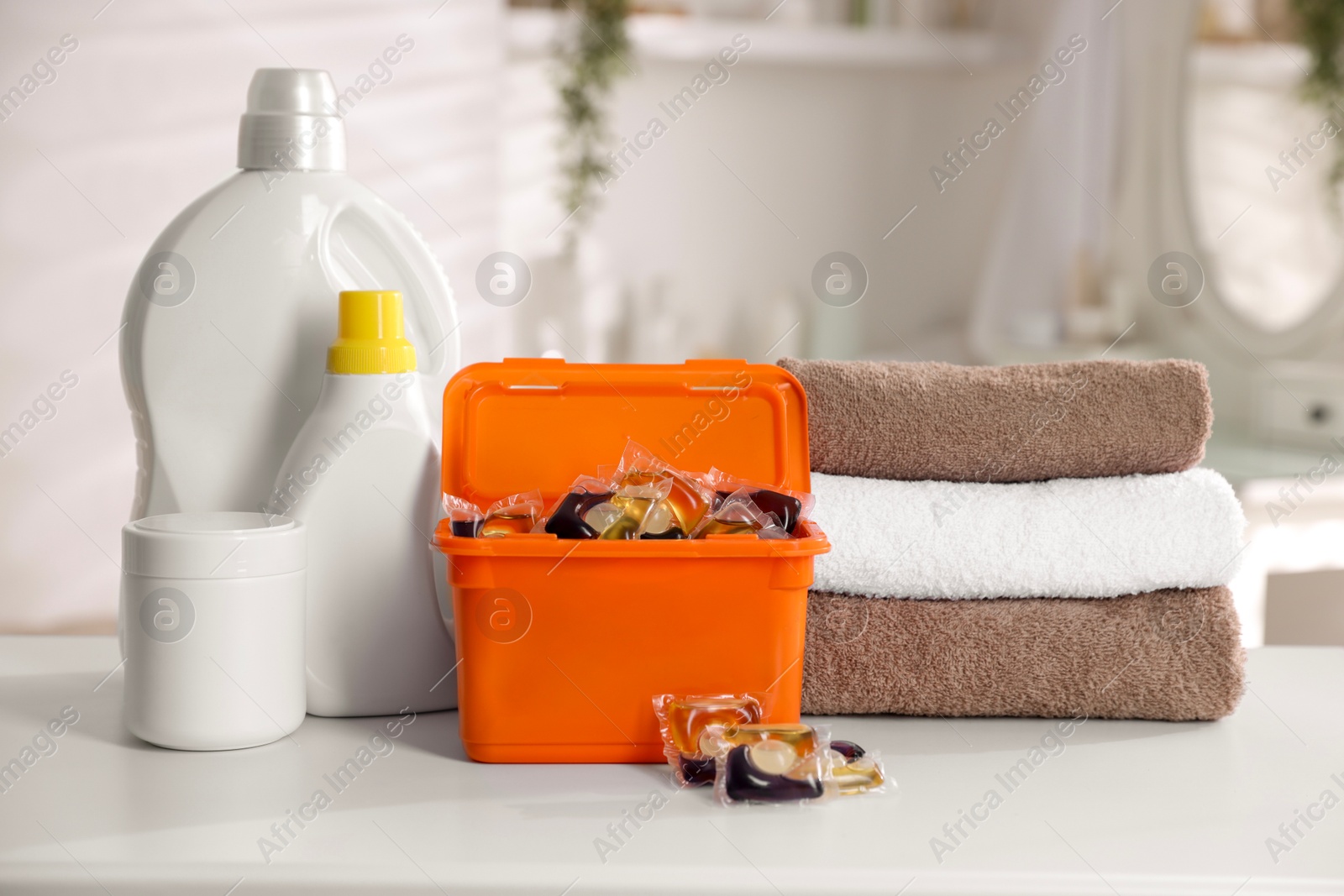 Photo of Laundry capsules, detergents and clean towels on white table in bathroom