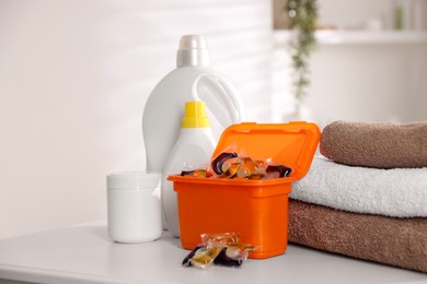 Photo of Laundry capsules, detergents and clean towels on white table in bathroom